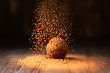 Delicious chocolate truffles sprinkled with cocoa on a black reflective background.