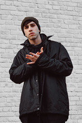 A young man wearing black winter clothing. A handsome young guy wearing black outfit. Man against white brick wall.