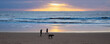 Couple with dog walking on sunlit beach at sunrise. Blyth, Northumberland, England, uk.