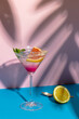 Vertical image of glass of cocktail over beige and pink surface with shadows