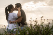 © PhotoFL - Young couple in love hugging and kissing in a natural environment with flowers. Couple giving each other affection and love in the mountains with sunset in the background.