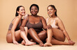© Nina L/peopleimages.com - Diversity, women friends and body portrait with skin glow group together for inclusion, beauty and power. Underwear model people on beige background with a smile, pride and motivation for self love