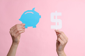 Wall Mural - Female hands holding paper-cut piggy bank and dollar symbol on pink background