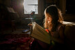 © Cavan Images - A small child sits in patch of bright sunlight reading a large book