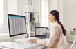 © Studio Romantic - Side view of a girl making audit, accounting or financial report, looking at large monitor. Attractive young woman is sitting in bright office at workplace at desk with laptop in front of the window.