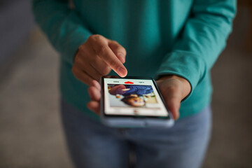 Close up of african american woman's hands putting red heart button giving like to a man's photo on her mobile dating application. Find love and online dating concept. Selective focus.