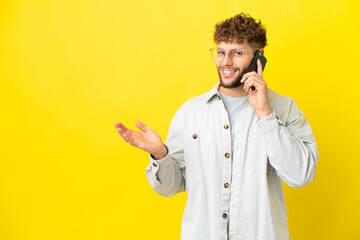 Poster - Young handsome caucasian man isolated on yellow background keeping a conversation with the mobile phone with someone