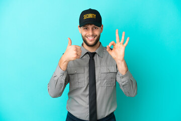 Wall Mural - Young security man isolated on blue background showing ok sign and thumb up gesture