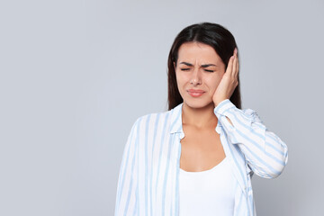 Sticker - Young woman suffering from ear pain on light grey background, space for text