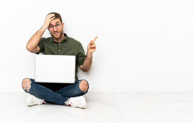 Canvas Print - Young man sitting on the floor surprised and pointing finger to the side