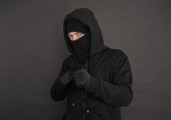 Wall Mural - Unrecognizable man in the black hoody with hood wearing balaclava mask holding his fists near chest