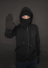 Wall Mural - Unrecognizable man in the black hoody with hood wearing balaclava mask holding hand up