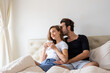 © Avirut S. - Couple relaxing on bed at home. Lover cuddling and embracing while sitting in bed in the morning. Romantic couple sitting on bed in bedroom. Young married Couple relaxing in bed with hot drink.