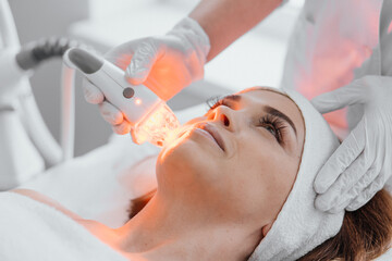 Red LED treatment. Woman doing facial skin therapy. Radiofrequency face lifting. Hardware antiaging procedure. RF lifting and vacuum massage. A cosmetologist performs a cosmetology procedure