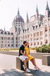 © Ivan - happy couple of man and woman tourists hugging while sitting near the parliament in Budapest. Travel for two. Honeymoon