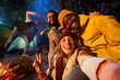 © CarlosBarquero - Mobile selfie of Multiracial smiling friends in the forest camping. Young adults with traveling spirit spending time in the countryside at night. Group of happy cheerful colleagues outdoors.