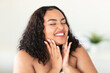 Attractive happy black body positive woman touching her smooth flawless skin on cheeks and smiling with closed eyes