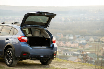 Blue off road car with open trunk lid at dawn on grassy hill on distant foggy city landscape background