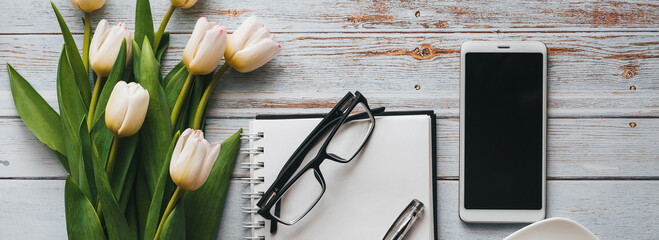 white bouquet of tulips on blue wooden background with coffee cup, a smartphone and an empty noteboo