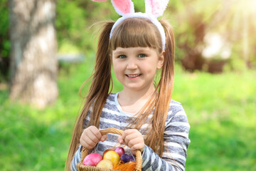 Poster - Little girl with Easter eggs in basket and bunny ears in spring park