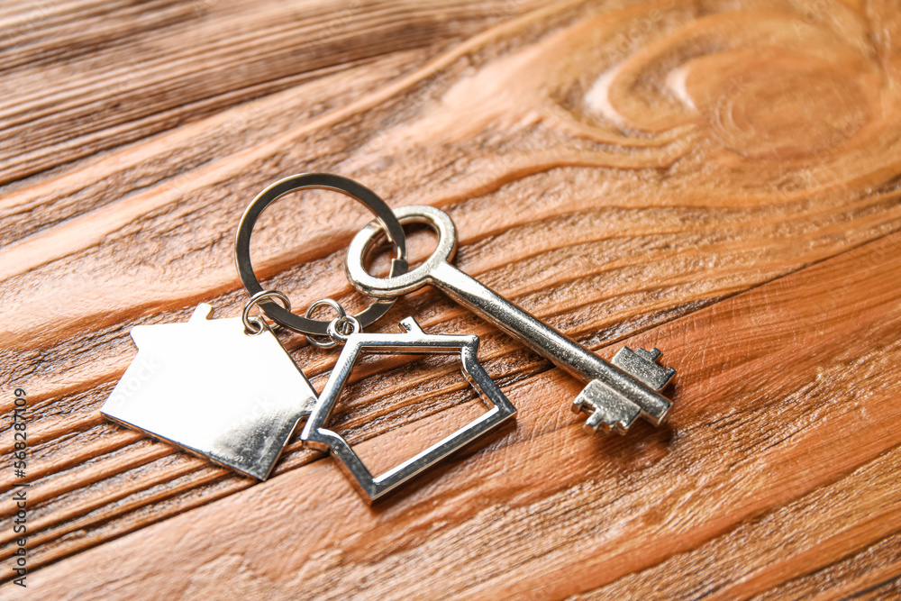 Key with house shape keychain on wooden background