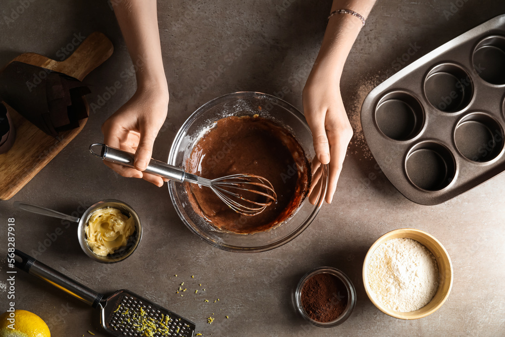 Woman preparing delicious chocolate muffins on dark background