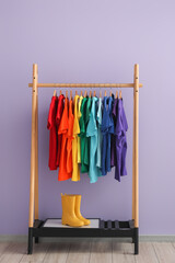 Wall Mural - Rack with colorful t-shirts and gumboots near lilac wall