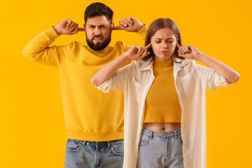 Wall Mural - Young couple suffering from loud noise on yellow background