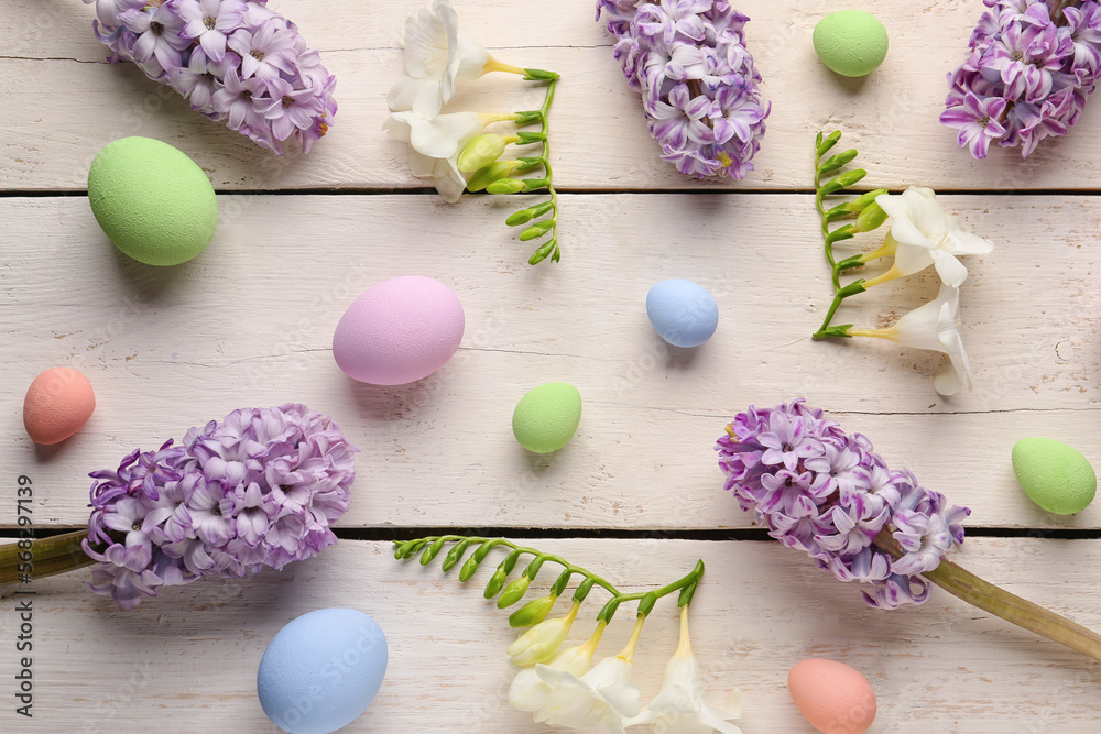 Composition with beautiful spring flowers and painted Easter eggs on light wooden background