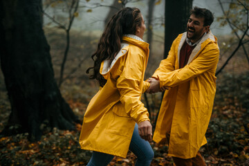 Loving couple in raincoats holding hands and having fun during a foggy day in the forest.