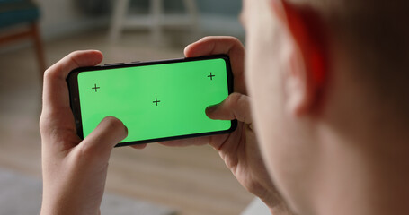 Wall Mural - Close up shot of man playing video games on his smart phone with chroma key green screen, quickly tapping on display - connection, technology concept 