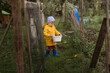 © Cavan Images - Boy in yellow raincoat walking with white basket in garden