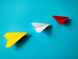Wall Mural - Red paper airplane origami leading white and yellow airplanes on blue background with customizable space for text. Leadership skills concept.