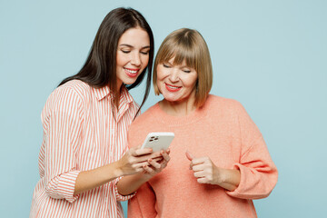 Wall Mural - Smiling happy cool fun elder parent mom with young adult daughter two women together wear casual clothes hold in hand use mobile cell phone isolated on plain blue cyan background. Family day concept.