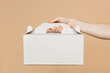 © ViDi Studio - Close up cropped male holding in hand hold cake dessert in unmarked clear empty blank white cardboard box isolated on pastel plain light beige color wall background studio. Service concept concept