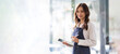 © Natee Meepian - Beautiful asian young barista woman in apron holding tablet and standing in front of the door of cafe with open sign board. Business owner startup concept.