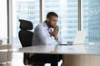 © fizkes - Serious young African business man looking at laptop screen, sitting at urban office work table against big window, watching Internet project presentation, webinar, talking on video call