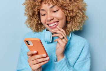 Wall Mural - photo of cheerful curly haired woman smiles gently focused at smartphone screen glad to receive noti