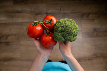 Wall Mural - Female hands hold tomato, broccoli on the background of a wooden floor. Top view, flat lay