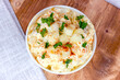 Fresh homemade traditional old-fashioned Amish Potato Salad with potatoes, boiled eggs, creamy dressing and celery in a white bowl on wooden background top view.