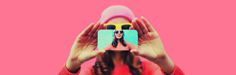 Close up of modern young woman stretching her hands taking selfie with smartphone on pink background
