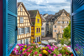 Wall Mural - View from an open window overlooking a small square with cafes and half timber frame buildings in the medieval historic center of Colmar, France.