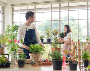 gardener young Asian man woman two person stand and sit chair smiling looking hand holding help decorate the tree leaf green in calm work shop home plant white wall. hobby job happy and care concept