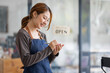 © David - Shot of smiling young cafe show owner Asian woman standing with arms crossed and Open sign on the glass door. Portrait of asian tan woman barista cafe SME entrepreneur seller business concept.