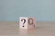The wooden cube block with an illustration magnifying glass to analyze the question mark sign is isolated on the table. Problems and root cause analysis concept. Define problems to find solutions.