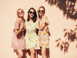 Three young beautiful smiling hipster female in trendy summer dress clothes. Sexy carefree women posing in the street. Positive models having fun outdoors at sunny day. Cheerful and happy. Near wall
