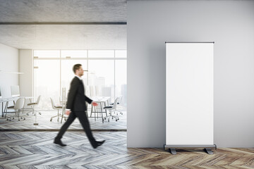 Poster - Businessman walking in modern glass office interior with empty mock up banner on wall, wooden flooring, furniture, window with city view and other objects.