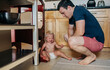 © Cavan Images - Dad looks down at diapered toddler girl while crying in kitchen