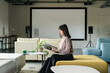 © Westend61 - Woman sitting on couch in lounge room looking at catalgue