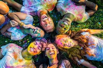 Multiethnic group of happy playful friends playing and having fun with holi colorful powder at the park